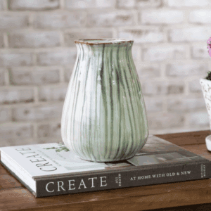 Elegant green ceramic vase on stacked books with rustic background.